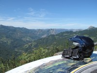 A motorcycle helmet and gloves rest on a panoramic guide at a lookout point in the Spanish mountains