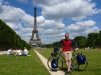 A biker (not sunburnt at all) stands in front of the Eiffel Tower with a blue bike
