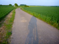Shadow of a cyclist cast on a quiet lane running through open fields in the English countryside