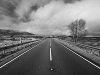 Black and white photo from the centre of a long, straight road as it snakes off towards the horizon
