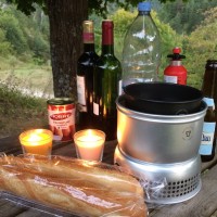 Two candles, some bottles of wine, and a cooker wait on picnic table
