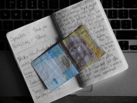 A colourful Ukrainian banknote holds place in a black and white notebook resting on the keyboard of a small Apple laptop