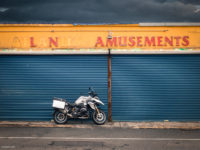 Bike parked in front of shuttered amusement arcade, rusty signage and totally realistic clouds in background.