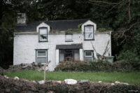 Front view of a derelict dwelling in front of which stands a sign bearing the words Rock Cottage