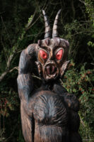 Image of a wooden carved figure with glowing red eyes and the horns of a goat